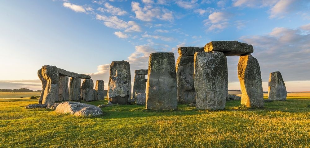 Stonehenge at sunset with blue sky and clouds in the background.
