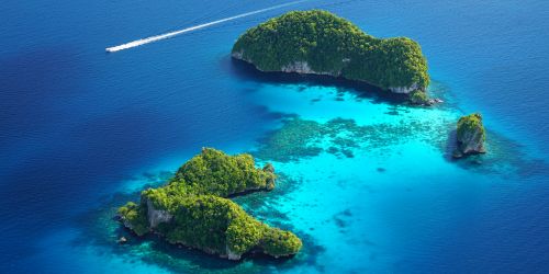 Aerial view of lush green islands surrounded by turquoise waters with a boat leaving a white wake.