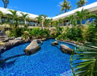Lush tropical hotel garden with a vibrant blue pool surrounded by palm trees and plants.