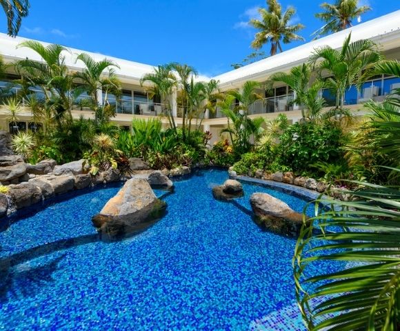 Lush tropical hotel garden with a vibrant blue pool surrounded by palm trees and plants.