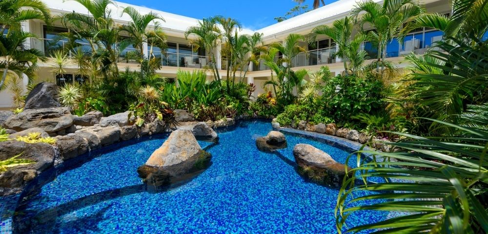 Lush tropical hotel garden with a vibrant blue pool surrounded by palm trees and plants.