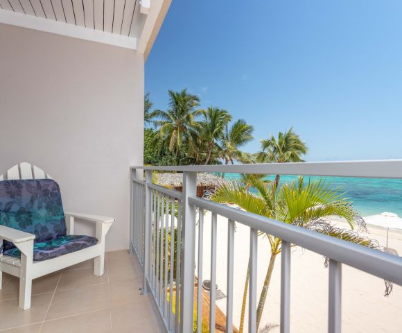 Balcony with a chair overlooking a tropical beach with palm trees and clear blue sea at Moana Sands Beachfront Hotel by My Holiday.