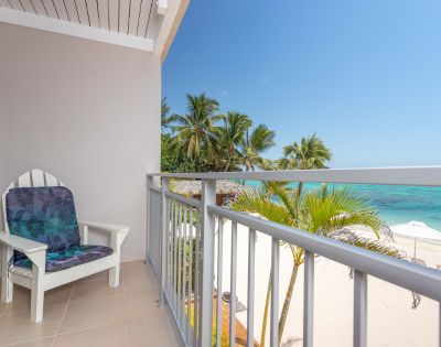 Balcony with a chair overlooking a tropical beach with palm trees and clear blue sea at Moana Sands Beachfront Hotel by My Holiday.
