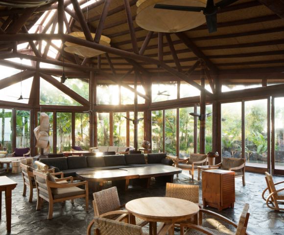 Sunlit tropical resort lounge with wicker furniture and wooden beam ceiling. Coconuts Beach Club Resort and Spa, Samoa.