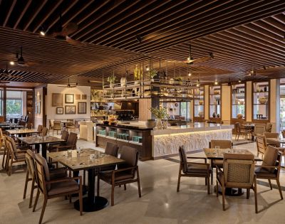 Elegant café interior with wooden tables, chairs, bar counter, pendant lights, and decorative ceiling.