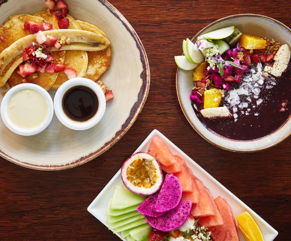Assorted breakfast plates with pancakes, fruit, and acai bowl.