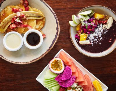 Assorted breakfast plates with pancakes, fruit, and acai bowl.