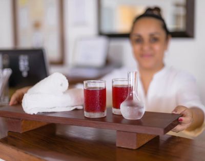 Person holding a wooden tray with two glasses of red drink and a white towel.