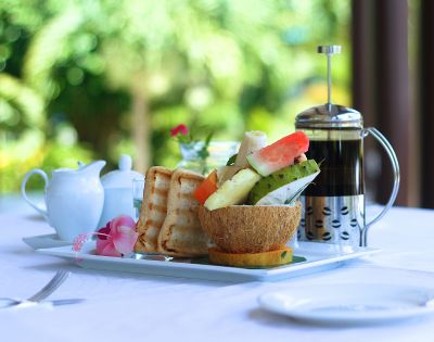 A breakfast tray with toast, fresh fruit in a coconut bowl, a French press, and a milk jug.