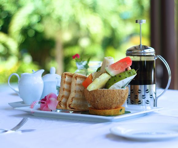 A breakfast tray with toast, fresh fruit in a coconut bowl, a French press, and a milk jug.