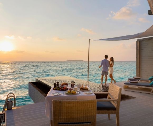 A couple enjoying a sunset by an infinity pool with a dinner table set nearby.