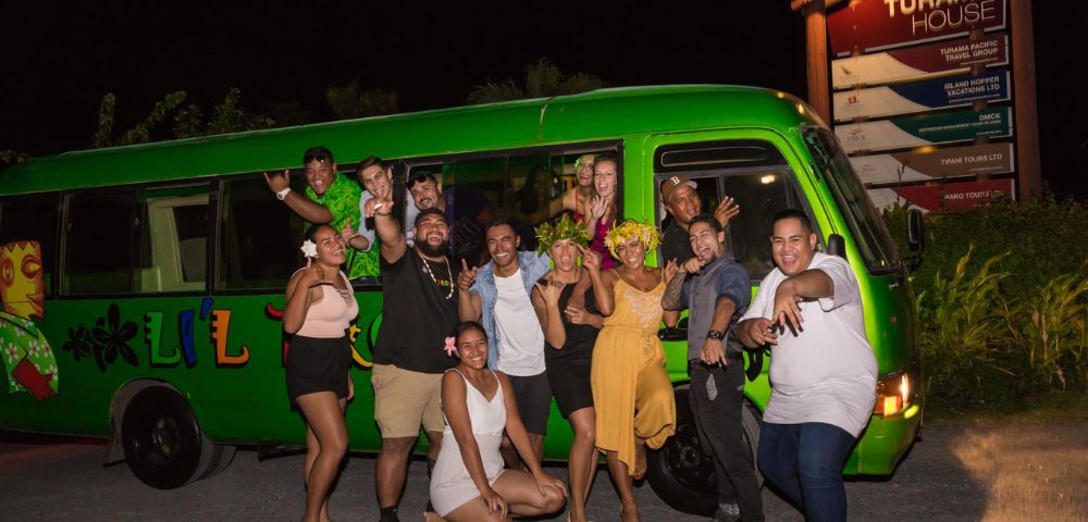 Group of people celebrating next to a green bus at night.