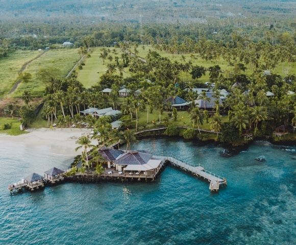 Aerial view of a coastal resort with pier surrounded by trees and clear blue water.