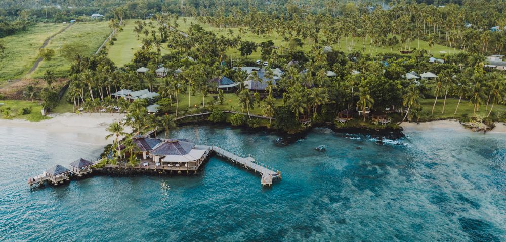 Aerial view of a coastal resort with pier surrounded by trees and clear blue water.