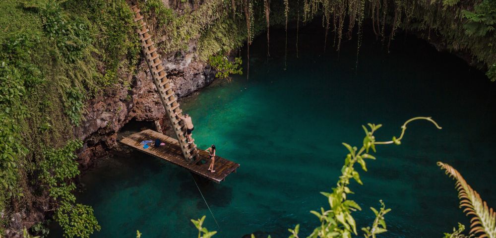 Wooden platform with a ladder over a serene blue water hole, surrounded by lush greenery.