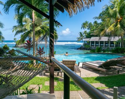 Tropical resort view with a hammock, palm trees, a pool, and the ocean in the background.