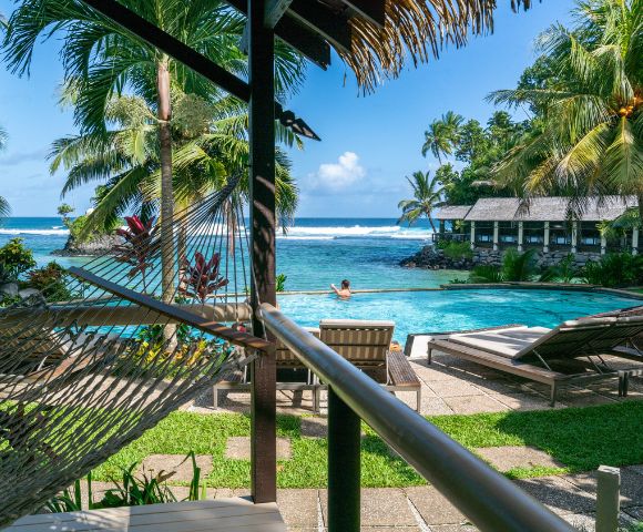Tropical resort view with a hammock, palm trees, a pool, and the ocean in the background.