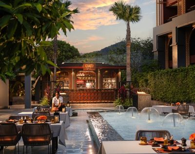 Outdoor dining area by a water fountain with tables set for a meal at dusk.