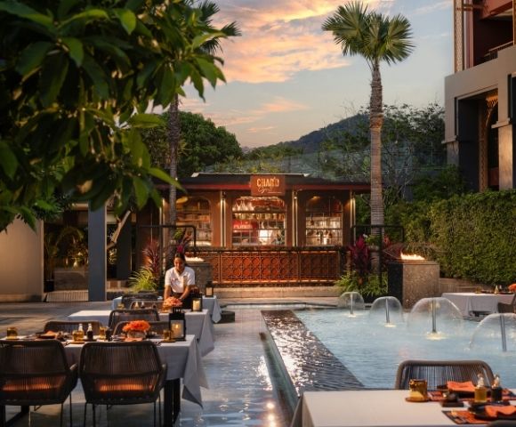 Outdoor dining area by a water fountain with tables set for a meal at dusk.