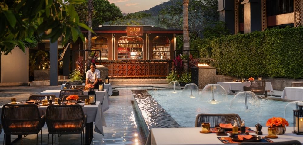 Outdoor dining area by a water fountain with tables set for a meal at dusk.