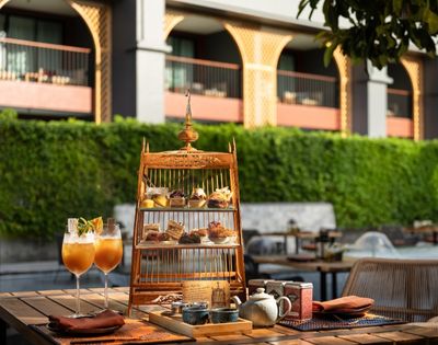 Outdoor table with a birdcage-shaped dessert stand, two cocktails, and hotel backdrop.