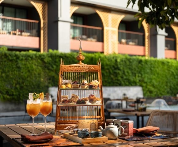 Outdoor table with a birdcage-shaped dessert stand, two cocktails, and hotel backdrop.