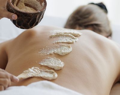 A masseuse wiping a body scrub onto a person's back.