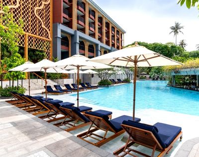 Poolside area with lounge chairs and umbrellas in front of a hotel.