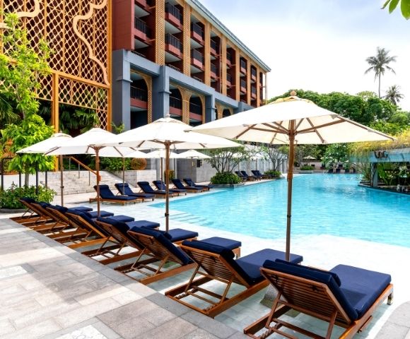 Poolside area with lounge chairs and umbrellas in front of a hotel.