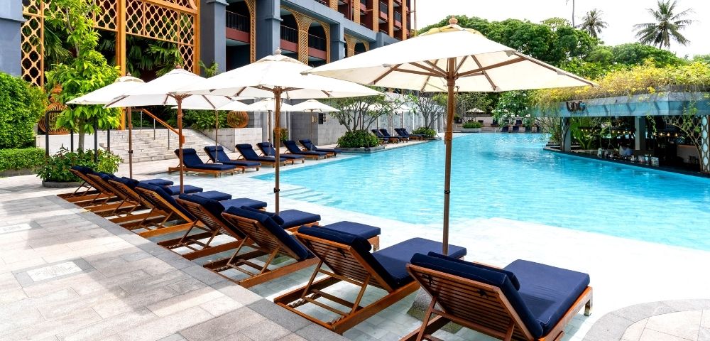 Poolside area with lounge chairs and umbrellas in front of a hotel.
