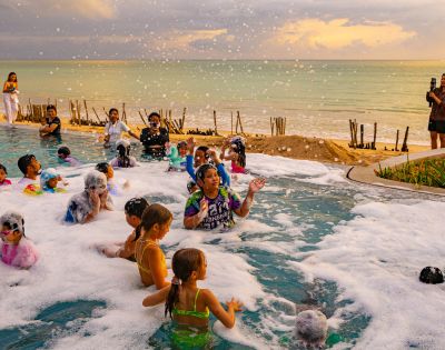 People enjoy a foam party by the sea at sunset.