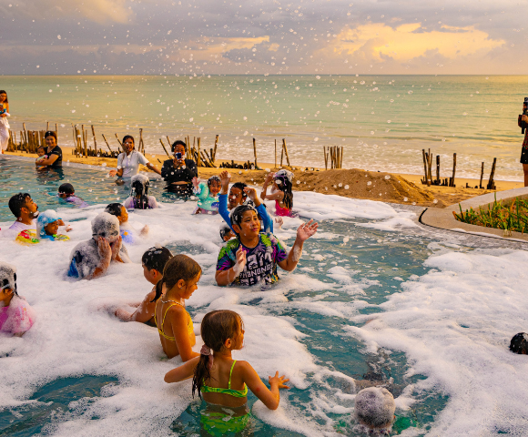 People enjoy a foam party by the sea at sunset.