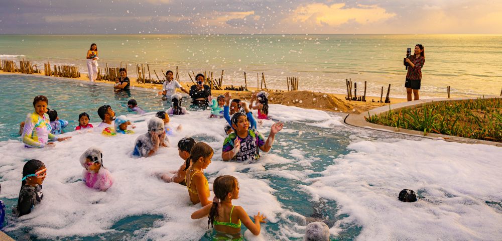 People enjoy a foam party by the sea at sunset.