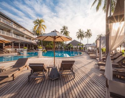 Luxury resort pool with sun loungers, umbrellas, and palm trees at sunset.