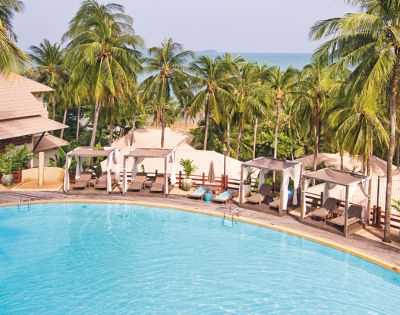 Tropical resort with a pool, sun loungers, and palm trees overlooking the ocean.