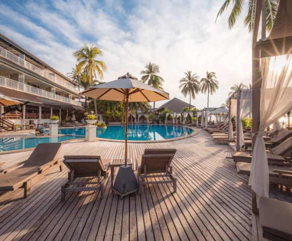 Luxury resort pool with sun loungers, umbrellas, and palm trees at sunset.