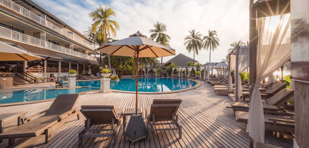 Luxury resort pool with sun loungers, umbrellas, and palm trees at sunset.