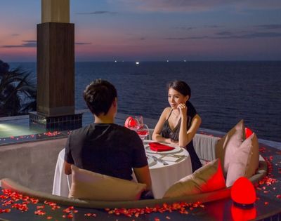 A couple at a romantic seaside dinner setup during dusk.