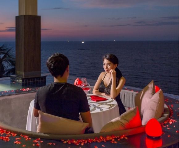 A couple at a romantic seaside dinner setup during dusk.