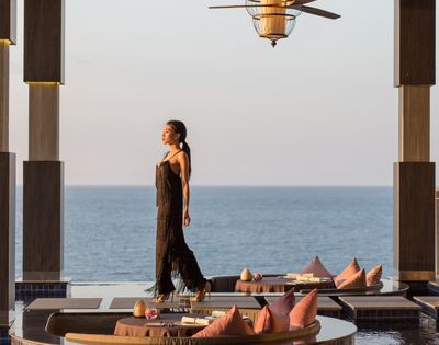 Woman in black dress walking by a seaside dining at sunset.