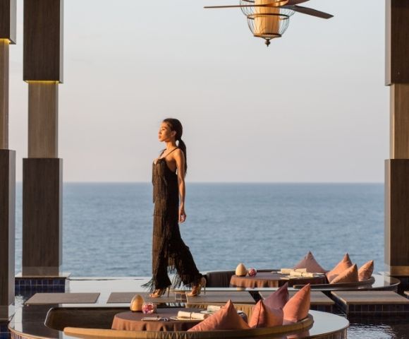 Woman in black dress walking by a seaside dining at sunset.