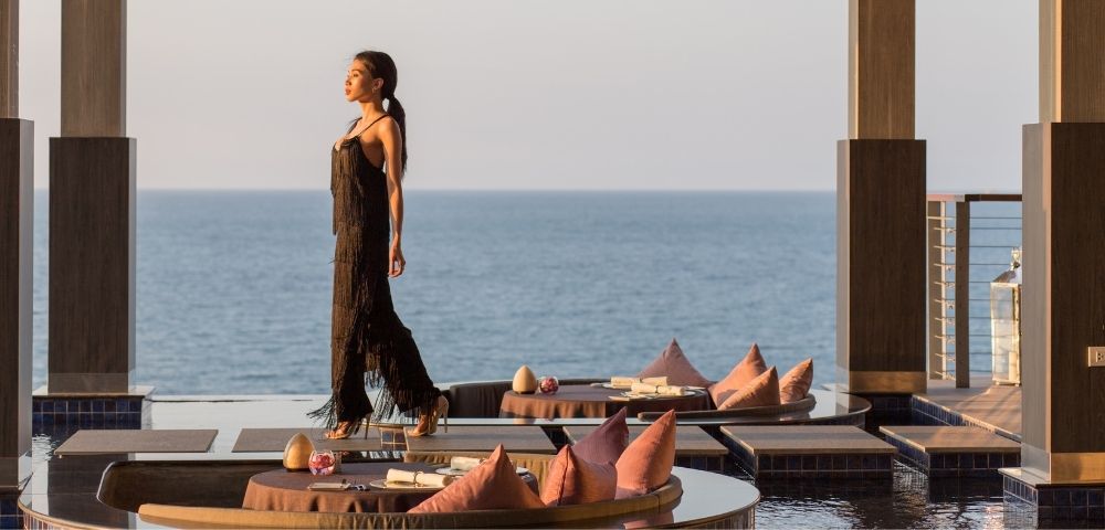 Woman in black dress walking by a seaside dining at sunset.