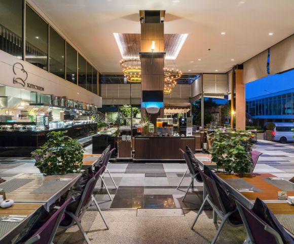 Modern hotel buffet area with dining tables, a food counter, and chic lighting at twilight.