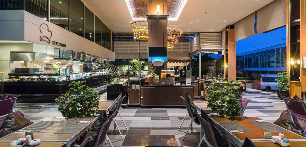 Modern hotel buffet area with dining tables, a food counter, and chic lighting at twilight.