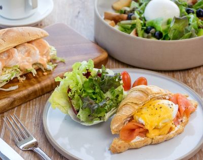 A breakfast plate with a croissant sandwich topped with an egg and smoked salmon, served with a side salad.