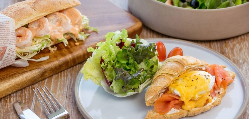 A breakfast plate with a croissant sandwich topped with an egg and smoked salmon, served with a side salad.