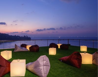 Outdoor lounge with bean bags and lamps on grass overlooking the sea at dusk.