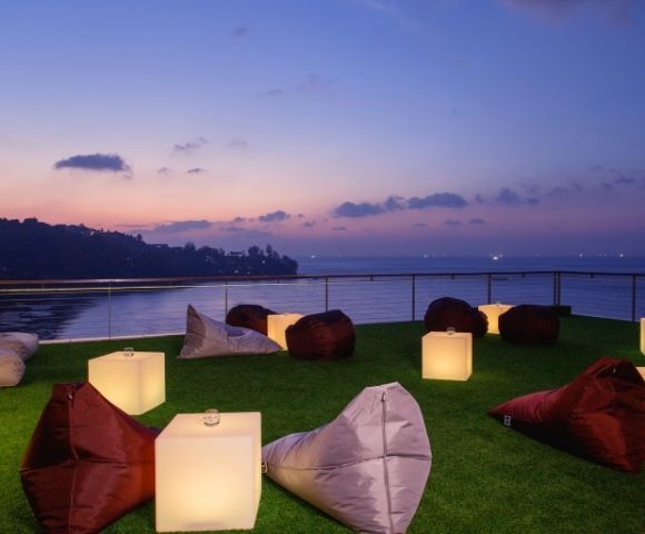 Outdoor lounge with bean bags and lamps on grass overlooking the sea at dusk.