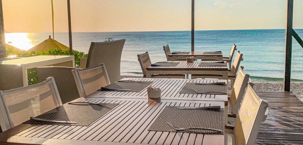 Seaside restaurant terrace with tables and chairs overlooking the ocean at sunset.