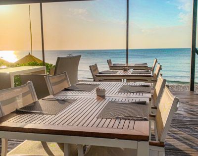 Seaside restaurant terrace with tables and chairs overlooking the ocean at sunset.